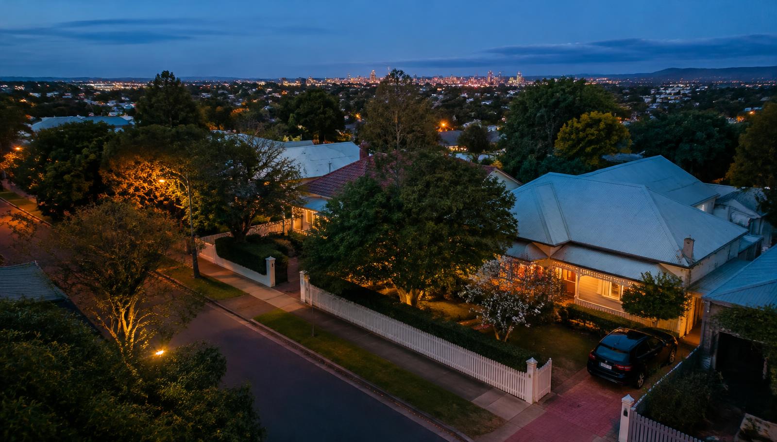 An eastern Adelaide street of heritage homes at dusk with the city skyline beyond