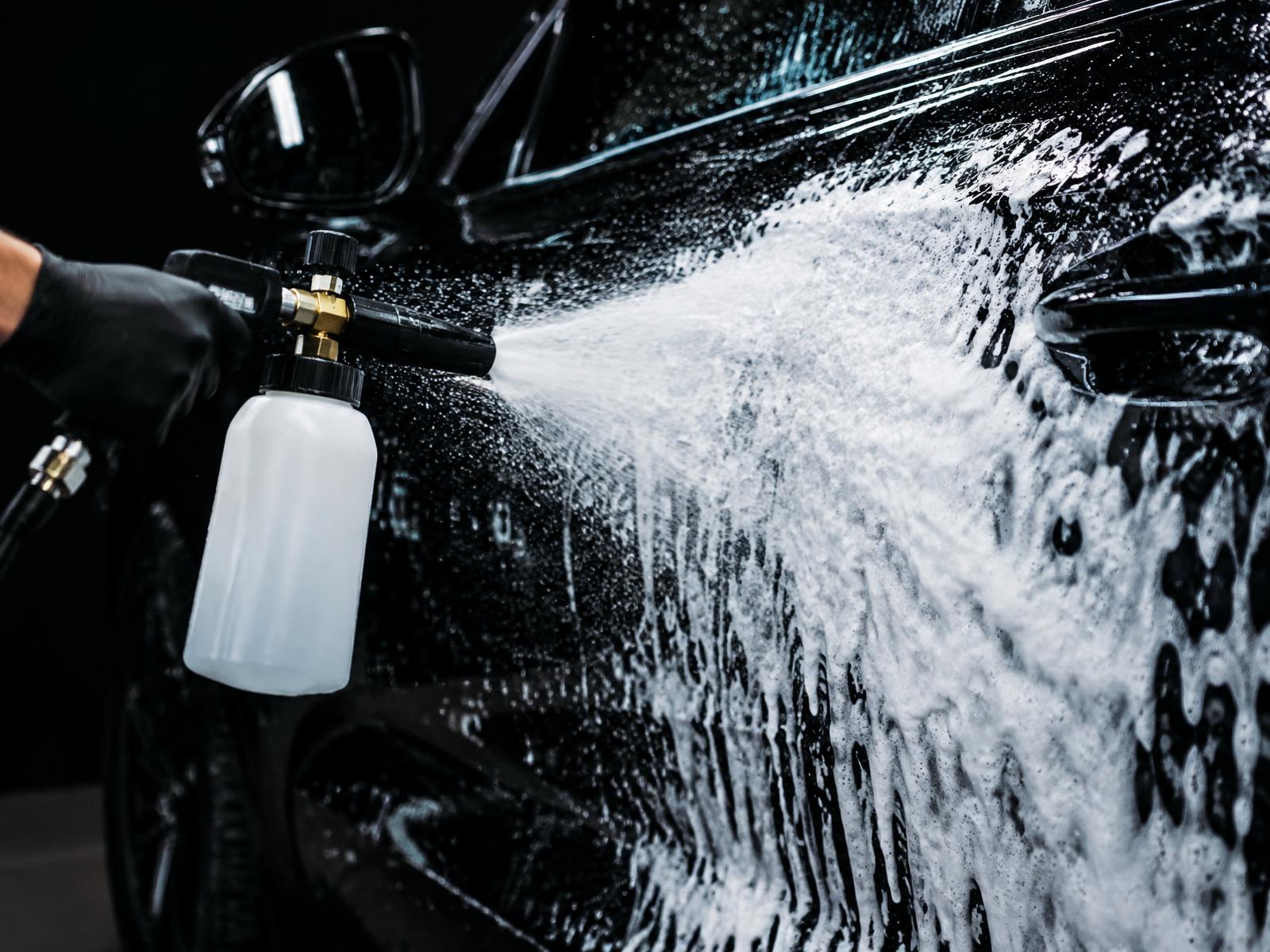 Thick white snow foam being applied to a glossy black vehicle during exterior detailing